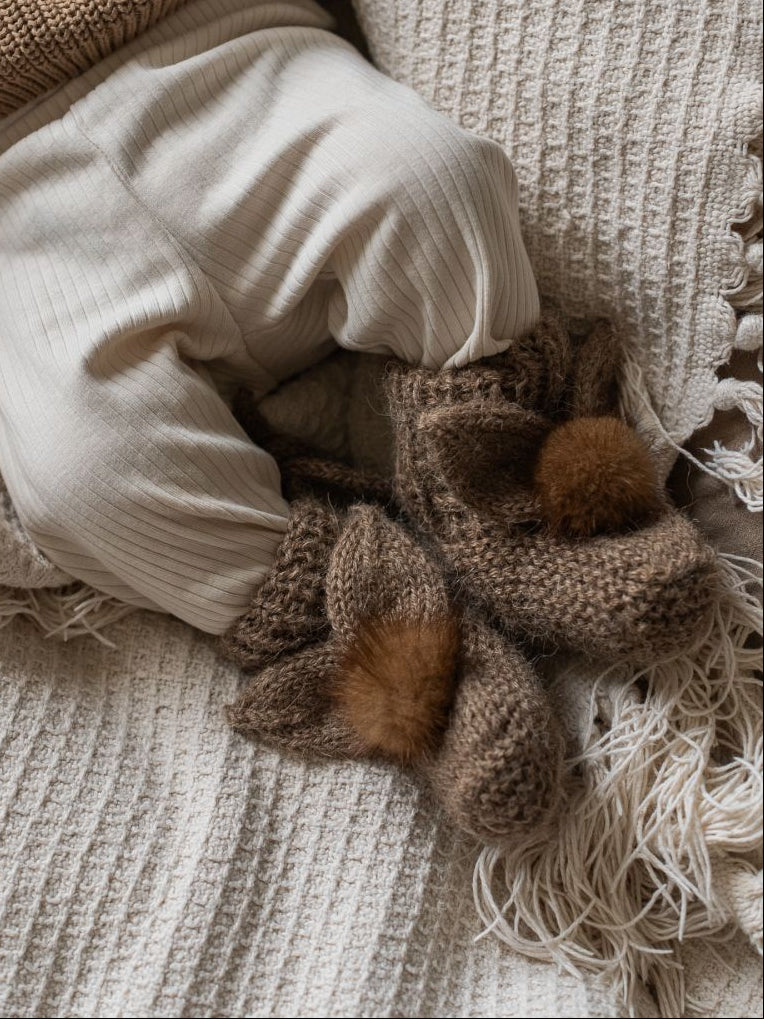 Baby in a brown knitted outfit with 'verte' text, lying on a textured blanket.